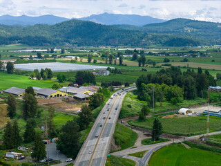 Fototapeta premium Aerial View Of Highway Cutting Through Farmland Valley With Mountains Near Abbotsford Mission BC, Canada