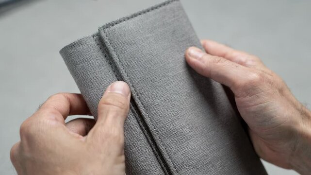 Closeup medium shot capturing fabric wrap application on a flexible notebook cover emphasizing texture alignment and seam detail during production.