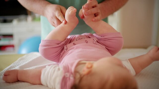 A colorful baby rattle is gently presented to an infant, while caregiver is performing mobility exercises