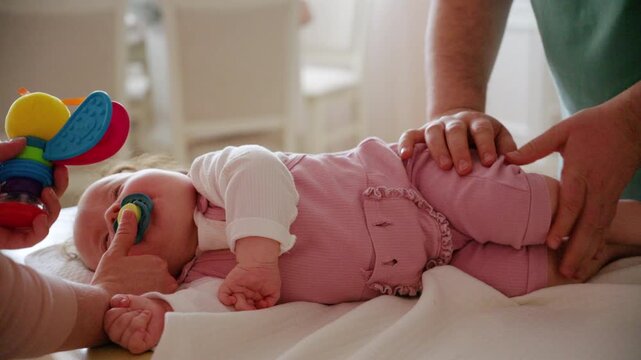 A colorful baby rattle is gently presented to an infant, while caregiver is performing mobility exercises