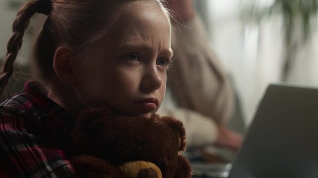 Caucasian upset little girl child hugging teddy bear crying busy father ignoring sad lonely daughter at home dad man male working laptop family conflict emotional distant relationship bad childcare