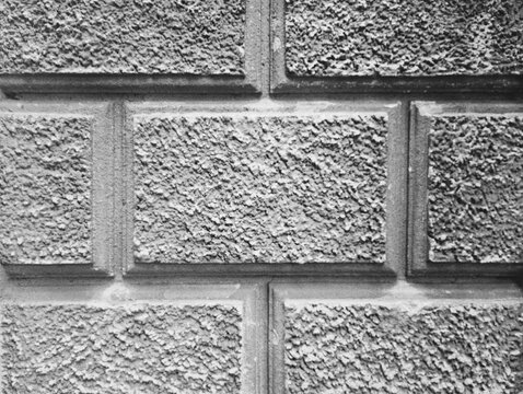 Monochrome close-up of a classic architectural facade featuring a textured rusticated wall plaster pattern. This high-quality black and white photograph highlights decorative geometric relief blocks, 
