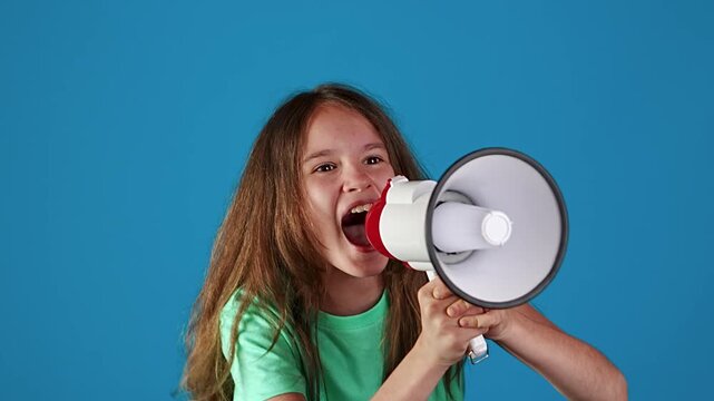 Young pretty teen girl yelling through megaphone against blue background