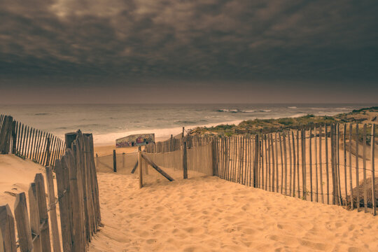 Creative fine art coastal landscape in Labenne Ocean with an artistic beach access path through sand dunes and wooden fences under a cloudy sky, scenic sunset views in Landes.