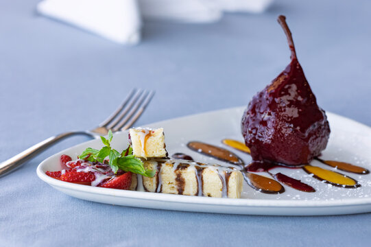 Poached pear dessert with sponge cake slices and fresh strawberries on white plate