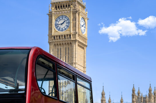 A close up of a traditional red double decker sightseeing tour bus with the historic Big Ben clock face and Elizabeth Tower rising behind under a blue sky in London England