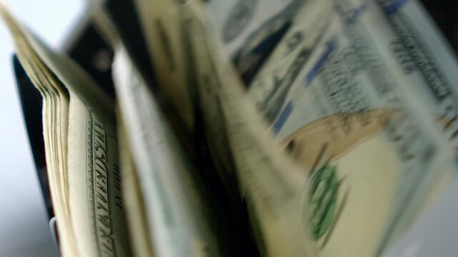 Banknotes emerge from a black cash register, showcasing intricate details and vibrant colors as sunlight dances on their surface, capturing the essence of commerce