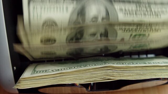 In a bustling office, a high-speed currency counter efficiently sorts stacks of cash, revealing hundreds of bills flowing smoothly through the machine, creating order from chaos