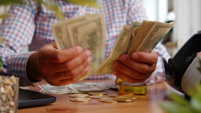 Hands skillfully count stacks of cash on a wooden desk, surrounded by coins, as sunlight pours in through windows, highlighting the vibrant office atmosphere