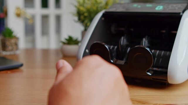 Hands glide over freshly printed bills as a smart machine swiftly counts and sorts the cash, illuminating the richness of financial organization in a warm workspace
