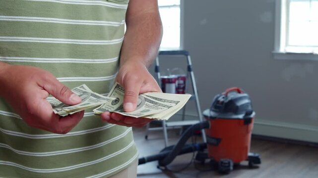 A man carefully counts dollar bills, assessing how much money he will need for home renovation materials. He looks determined to ensure everything fits within his budget