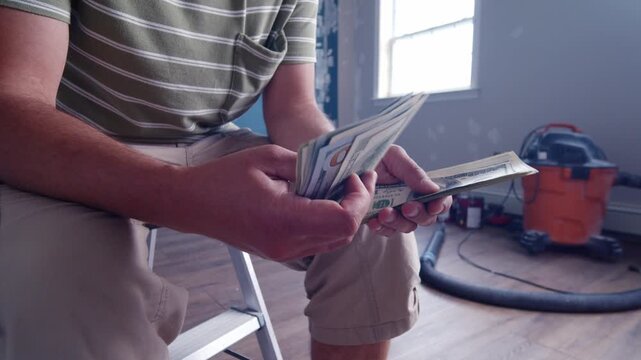 A man carefully counts dollar bills while planning expenses for home renovations. He considers how much to allocate for essential materials to improve his house