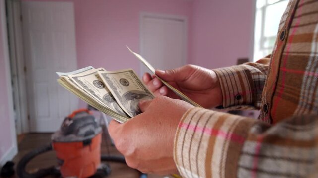 A man is carefully counting dollar bills to determine how much he needs for materials to fix up his home. The room has a warm, inviting atmosphere