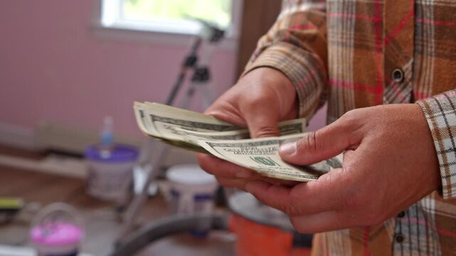 Focused on planning, a man carefully counts dollar bills to determine how much he will need for materials to refresh his home and enhance its comfort