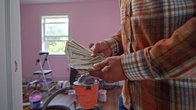 A man carefully tallies dollar bills, determining how much he needs for materials to transform his home. His focus reveals the excitement of renovation ahead