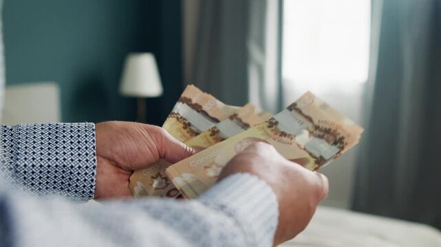 A man meticulously counts Canadian dollars in a serene room filled with natural light. Each bill reflects the craftsmanship and value, creating a moment of focus and calmness