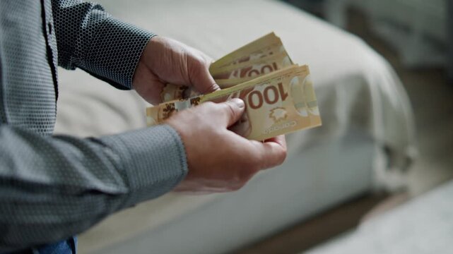In a serene room, a man's hands skillfully count Canadian dollars, showcasing crisp bills and focusing on the subtle details of finance and daily life