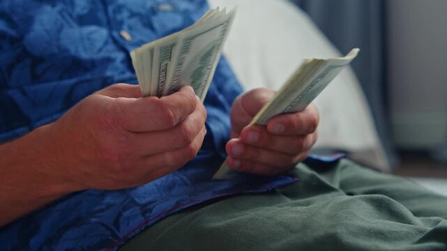 A person counts crisp dollar bills on a calm day, sitting on a soft bed in a cozy room, their hands revealing both excitement and thoughtfulness about future plans