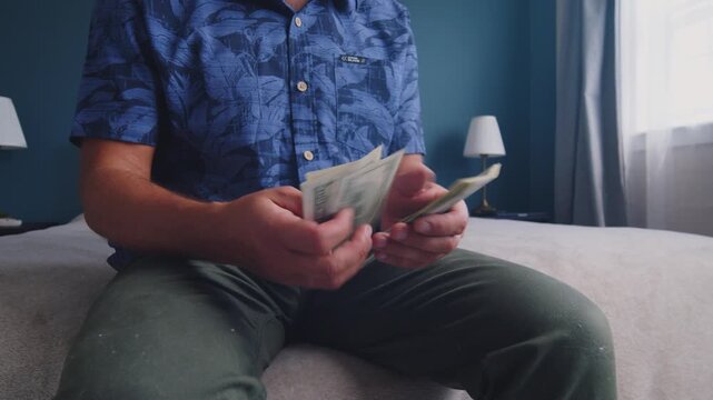 A man sits on a soft bed, carefully counting stacks of cash. The warm light creates a reflective atmosphere as he considers his financial situation