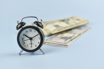 Silver alarm clock stands beside folded bills © Nazir
