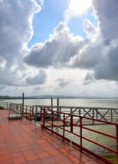 Obraz premium Metallic pier walkway with red handrail over the sea under a dramatic cloudy sky
