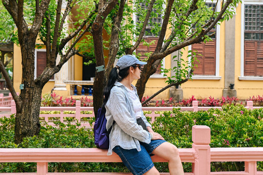 Mature 50 years old Russian woman tourist in cap looking away at beautiful Lou Lim Ioc Garden near historic pavilion in Macau travel destination
