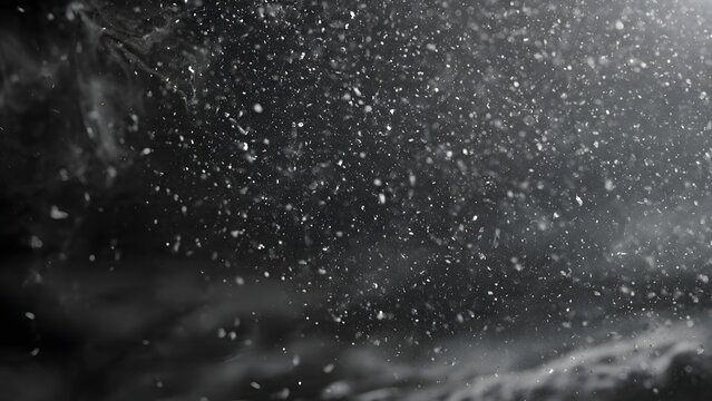 Black and white cinematic shot of fine white particles and dust motes floating in the air against a dark background with strong side lighting and soft bokeh effects.