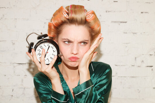 Funny portrait of young woman holding alarm clock. Time management and morning routine concept.