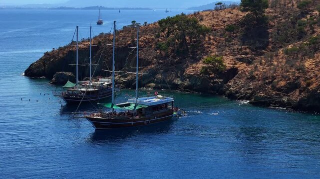 Aerial view of traditional gulet boats anchored near a rocky coastline in clear turquoise water, ideal for summer travel, coastal tourism, sailing, vacation and Mediterranean lifestyle content.