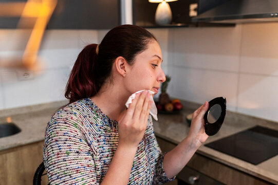 Makeup enthusiast cleansing her skin with a cotton pad while holding a hand mirror
