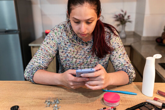 Costumed performer studying a makeup tutorial on her phone at a kitchen table