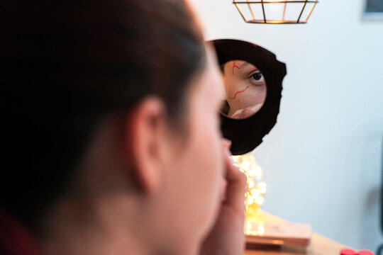 Reflection of a painted bloodshot eye in a round hand mirror during makeup session