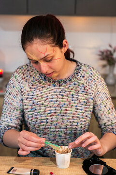 Young woman applying special effects scar makeup to her forehead at a home table