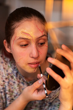 Costumed performer drawing red wound lines on her face with a fine liner brush