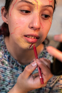 Close up of a redhead lining her lips in red over special effects facial wounds