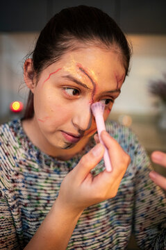 Profile of a costumed woman covering a scar wax wound with foundation at home