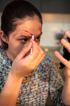Woman shaping a fake wounded eyebrow with an applicator for a Halloween costume