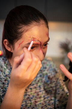 Redhead detailing a special effects brow wound with a swab beside a hand mirror