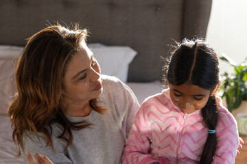 Mother and daughter sitting on bed in bedroom, applying cream, wearing pink fleece, gray sweater © wavebreak3