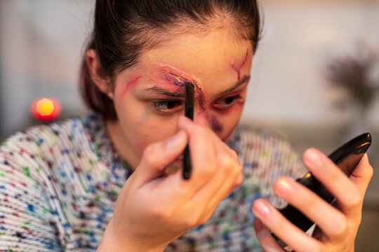 Costumed performer with stapled wounds adding detail near her nose at home