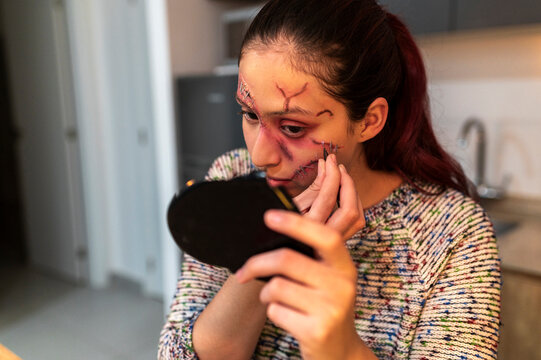 Redhead woman examining her special effects wounds in a small phone mirror