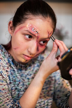 Costumed woman coating her lashes with mascara beside vivid facial wounds
