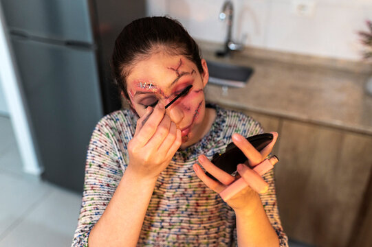 Costumed performer touching up makeup with a compact in a dim home kitchen