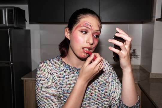 Young woman applying red lipstick while wearing horror special effects face makeup