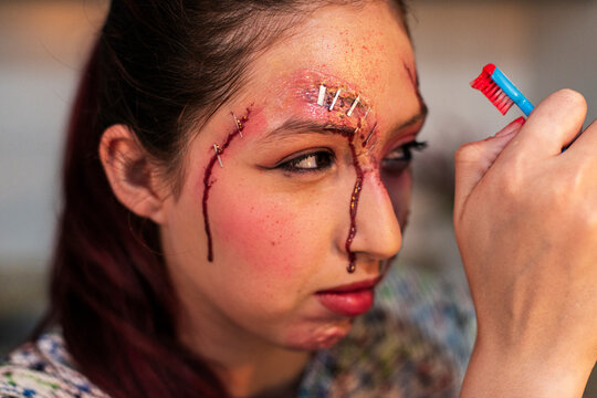 Sinister redhead character with bleeding wounds holding a small prop under flash