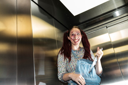 Wild killer doll character with raised arms grinning in a flash lit elevator