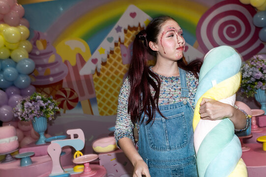 Creepy doll character cradling a plush toy in a rainbow candyland backdrop