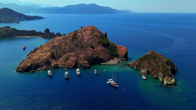 Aerial view of a rocky island surrounded by deep blue sea, turquoise bays and anchored boats, ideal for summer travel, coastal tourism, Mediterranean vacation and scenic nature projects.