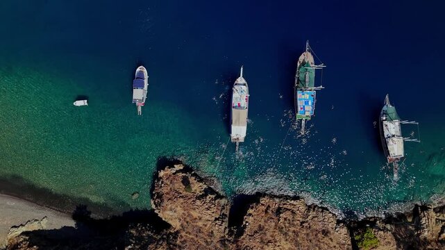 Aerial view of traditional gulet boats anchored near a rocky coastline in clear turquoise water, ideal for summer travel, coastal tourism, sailing, vacation and Mediterranean lifestyle content.