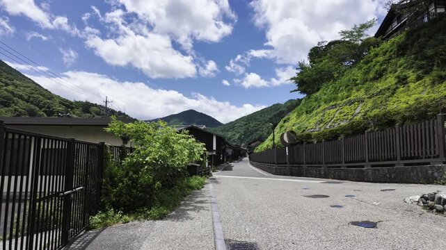A clear summer day, blue sky, white clouds. A small path leads to historic Narai-juku, with old-style houses on both sides.